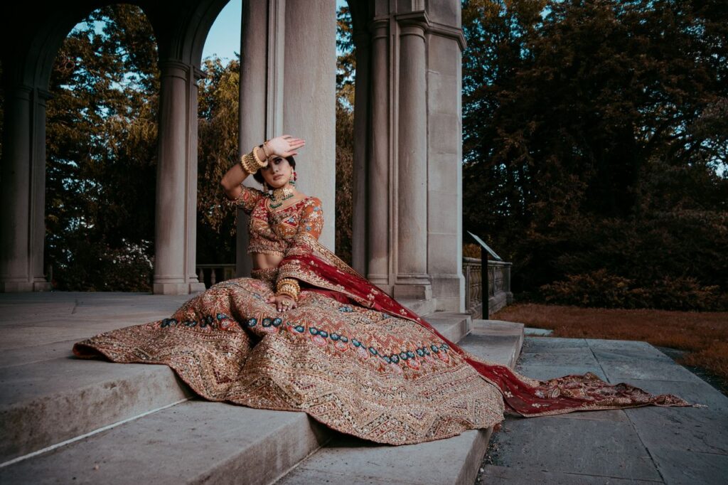 A bride in ornate traditional dress sits gracefully on stone steps in an outdoor setting.